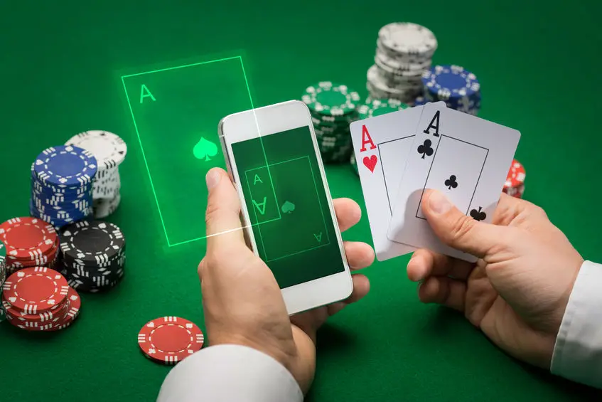 cassino, jogo online, conceito de tecnologia e pessoas - close-up do jogador de pôquer com cartas de baralho, smartphone e fichas na mesa de cassino verde